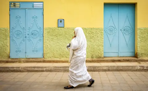 AFP A woman walks through the oasis town of Figuig - with yellow and blue painted walls and doors - on Morocco's border with Algeria - Saturday 20 March 2021