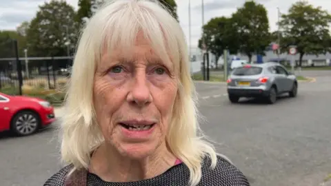 An older woman wearing a black and white top speaking from the side of a road in Bromley.