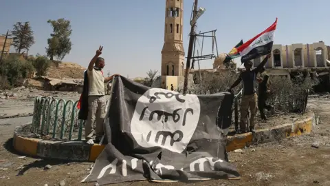 Getty Images Fighters from the Hashed al-Shaabi (Popular Mobilisation units), backing the Iraqi forces, pose with a flag of the Islamic State (IS) group in Tal Afar on 27 August 2017