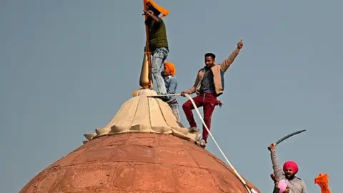 Getty Images Protesters climb on a dome at the ramparts of the Red Fort in Delhi