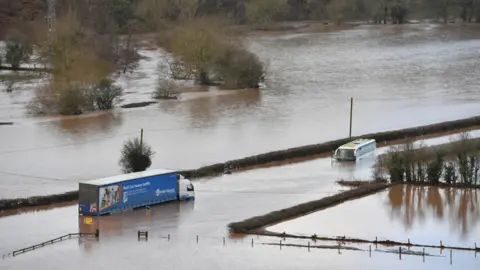 PA Media A lorry and a coach submerged in floodwater from the River Teme on the A443 near Lindridge, Worcestershire