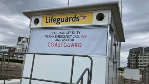 BBC The lifeguard provision on Bexhill beach with a 'Lifeguard off duty' sign on the front