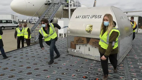 Getty Images UPS employees move one of two shipping containers containing the first shipments of the Pfizer and BioNTech COVID-19 vaccine a ramp at UPS Worldport in Louisville, Kentucky, on December 13, 2020.