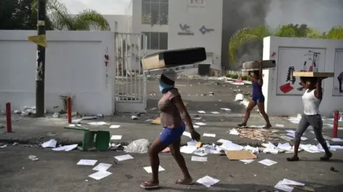 AFP In this file photo taken on July 7, 2018 People carry loot from a shop in the commune of Petion Ville during protest against the increase in fuel prices, in Port-au-Prince.