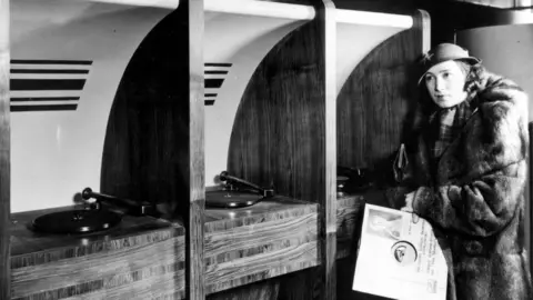 PA A woman at the first listening booths in HMV in the 1930s