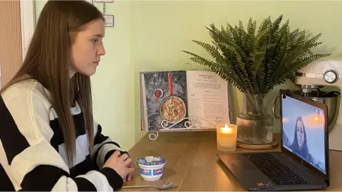 BBC Tia is sat in the kitchen with a laptop set up in front of her.