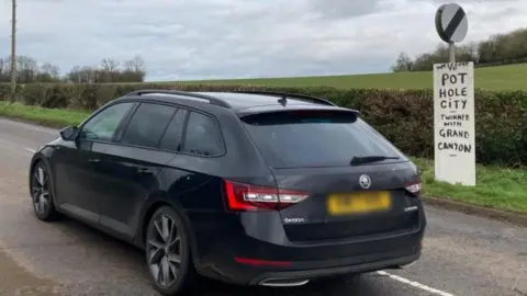 Martin Heath/BBC Car driving past a sign saying Welcome to Pot Hole City