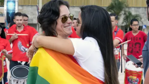 Getty Images A female couple hug each other wrapped in a pride flag outside the Supreme Court