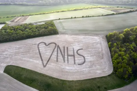 Chris Gorman / Big Ladder An aerial view on to a field in which NHS and a heart sign has been marked out using crops