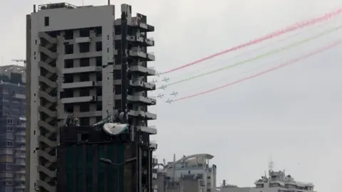 Reuters Aircraft fly past damaged buildings and release smoke in the colours of the Lebanese flag as French President Emmanuel Macron visits Lebanon, (1 September 2020)