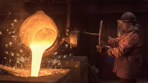 Worker pouring molten metal from flask in foundry workshop