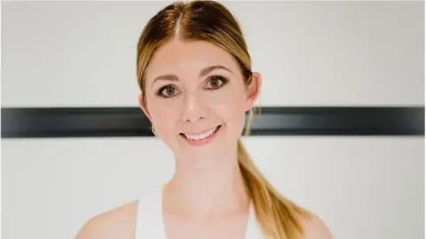 Nikki Franklin Nikki Franklin, smiling, stands against a mostly white background with a thick black band passing horizontally through the middle. Her hair is tied back in a long ponytail, and she's wearing a white vest top.