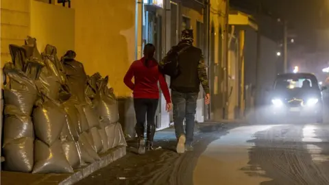 Getty Images Residents walk on ashes, past bags filled with ashes from the Mount Etna volcano stored aside after being swept by municipal employees from a street of Zafferana Etnea, north of Catania,