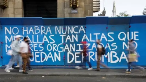 Reuters People walk past a barricade with a slogan reading "There will never be walls high enough that organised women can't overthrow" in Mexico City, Mexico March 7, 2021.