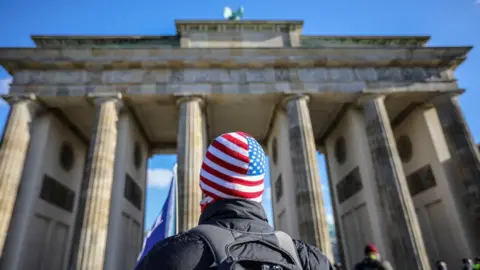 Getty Images A man in a US flag hat stands in front of Brandenburg Gate