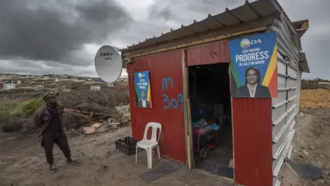 EPA A man stands outside an illegally erected shack on unstable sand dunes in Monwabisi, Cape Town, South Africa, 18 September 2018. The area has seen thousands of illegal shacks being erected over the past months.
