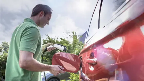 Getty Images Man charges red electric car