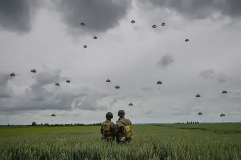 Christopher Furlong / Getty Images Military re-enactors look on as 280 paratroopers take part in a parachute drop onto fields at Sannerville on 5 June 2019 at Sannerville, France.