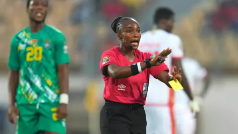Getty Images Rwandan referee Salima Mukansanga issuing a yellow card during the Guinea-Zimbabwe game in Yaoundé, Cameroon - Tuesday 18 January 2022