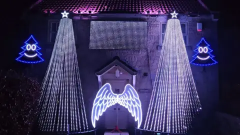 Family handout Image of the light display at Faye and Richard's home. There are two large Christmas trees made up of LED lights either side of their front door. There is also a pair of Christmas tree lights, which have smiley faces. LED Angel wings are placed on their front door.