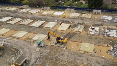 Steve Hubbard/BBC Drone footage shows a digger completing the demolition of new-build homes at Darwin Green in Cambridge