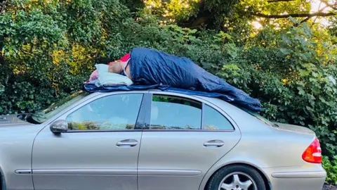 Two men sleep on top of a car