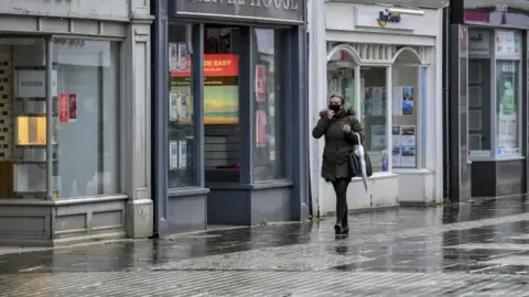 PA Media Woman walking past shops in Bridgend