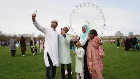 PA Media A family take a selfie with an observation wheel in the background, Cambridge, UK.