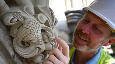 Finnbarr Webster Gary Price wearing a hard hat takes a close look at a stone carving