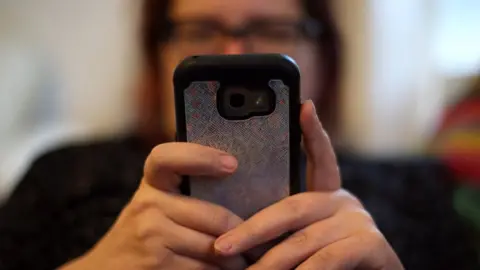 PA Media A woman using her mobile phone