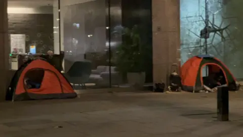 BBC Two orange tents and some belongings on a street next to an office in central London.