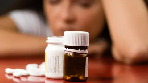 Getty Images A woman looks at a bottle of pills