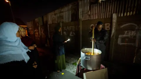 BBC/Shiraaz Mohamed Sheikh Sameeg stirring a large pot of food in Manenberg, Cape Town - South Africa