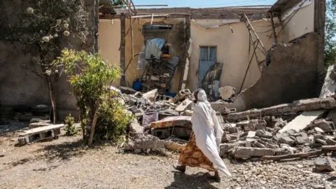 AFP A woman walks in front of a damaged house which was shelled as federal-aligned forces entered the city, in Wukro, north of Mekele, on March 1, 2021
