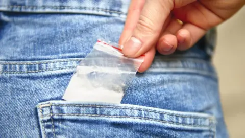 Getty Images Young person slips a bag of drugs into his back pocket