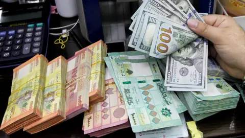 Reuters A man counts US dollars next to Lebanese pounds at a foreign exchange shop in Beirut, Lebanon (24 April 2020)