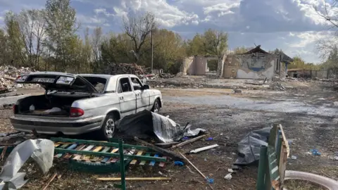 Scarlett Barter/BBC Debris of a car and buildings in Hroza after a missile strike killed 52 people