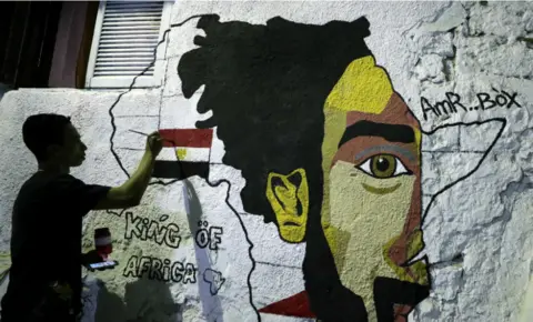 EPA On Monday, a man is seen daubing paint onto a mural which depicts Mo Salah, the outline of the African Continent, and the Egyptian flag.
