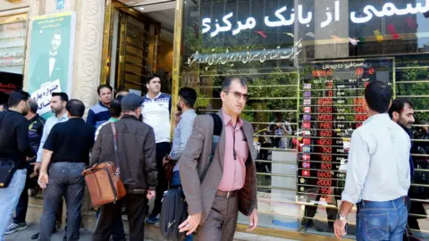 EPA Iranians check foreign currency rates at a shop in Tehran on 10 April 2018