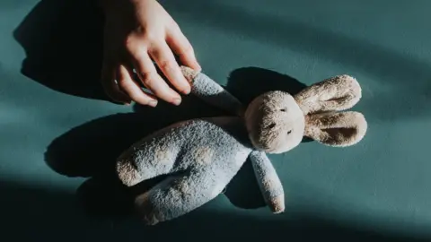 Getty Images Child's hand holding a teddy bear