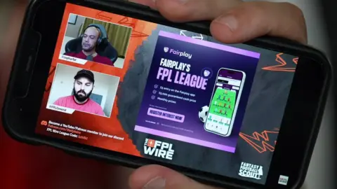 A phone showing an advert while people play FPL