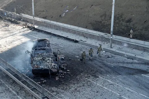 Reuters Ukrainian servicemen walk by a damaged vehicle, at the site of fighting with Russian troops, , in Kyiv, Ukraine February 26, 2022.