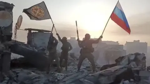 Reuters Wagner mercenary group fighters wave flags on top of a building in an unidentified location