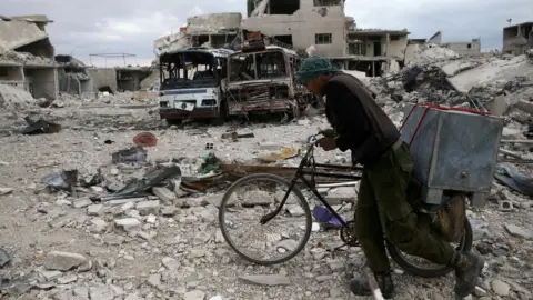 Reuters A Syrian man pushes his bike past destroyed buildings in the besieged rebel-held town of Douma on 30 March 2018