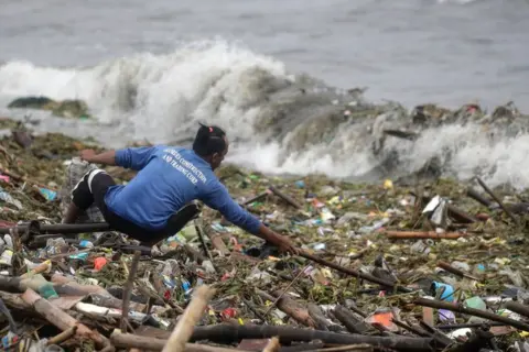 EPA A man collects washed up rubbish along the shore of Manila Bay, Philippines, 26 July 2023 during typhoon Doksuri