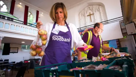 Neighbourly A woman wearing a purple apron working at a Foodbank