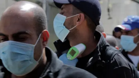 Palestinian medical workers check the temperatures of workers crossing at the Tarqumiya checkpoint, near the West Bank city of Hebron