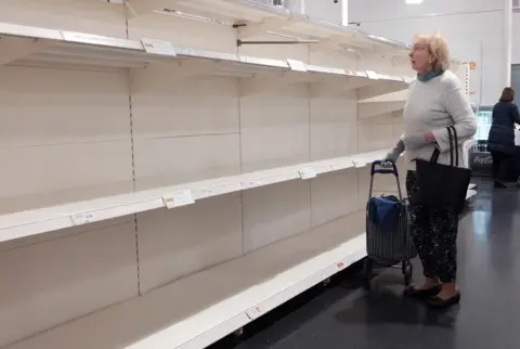 Yui Mok/PA A woman looks at empty shelves in a Sainsbury's store in London, 18 March 2020.