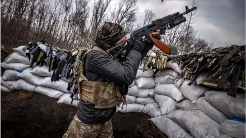 Getty Images A Ukrainian serviceman shoots at a Russian drone with an assault rifle from a trench at the front line east of Kharkiv