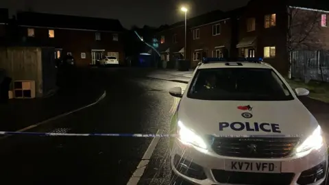 A police cordon and blue tent visible at the scene